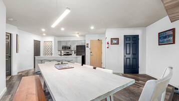 A modern kitchen with stainless steel appliances, a dining area with a long table and chairs, and a dark blue door.