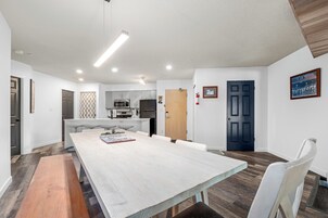 Una cocina moderna con electrodomésticos de acero inoxidable, un comedor con una mesa larga y sillas, y una puerta azul oscuro.