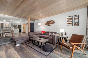 Uma sala de estar moderna com um sofá modular, uma mesa de centro, uma mesa lateral e uma obra de arte de parede com tema de árvore decorativa.