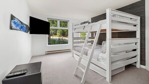 Una camera da letto con letti a castello, una televisione, una finestra che si affaccia sul verde e un telecomando su un tavolino.