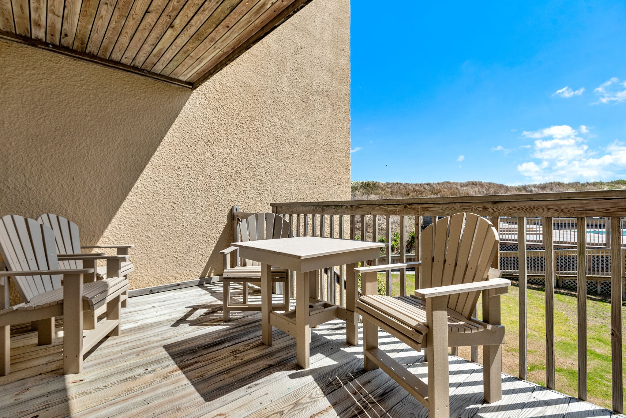 Eine Holzdar Terrasse mit Adirondack-Stühlen und einem Tisch, mit Blick auf eine Rasenfläche.