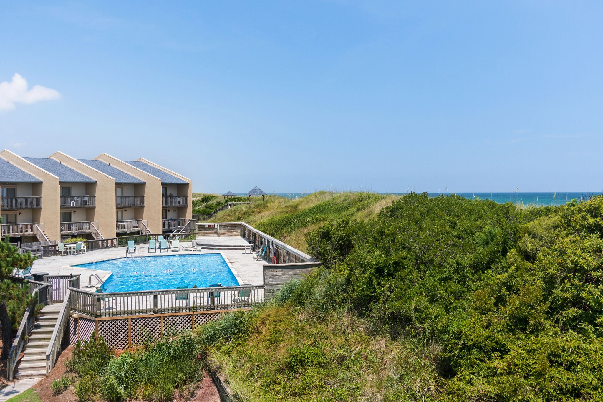 A pool area with a view of the ocean, surrounded by greenery and a building with balconies.