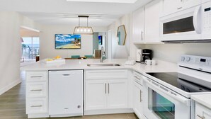Une cuisine moderne avec des meubles blancs, un lave-vaisselle, un four, un four à micro-ondes et un grand îlot central doté d’un évier.