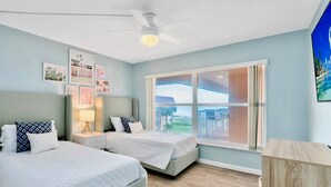 Une chambre avec deux lits, un ventilateur de plafond et une grande fenêtre donnant sur un beau paysage.