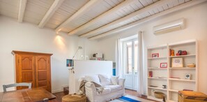 A room with a wooden dining table, a white sofa, a bookshelf, and a window with curtains.