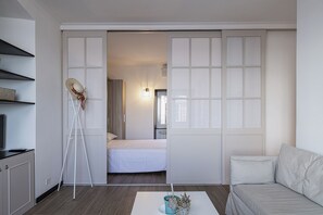 Une chambre à coucher de taille modeste, avec un lit, un canapé blanc et une petite table sur laquelle est posée une plante.