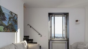 Ein modernes Wohnzimmer mit einer Couch, einem Sessel, einem Couchtisch und einem Fenster mit Meerblick.