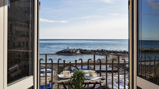 Ein Balkon mit Meerblick, ein Tisch mit Tasse und Untertasse sowie ein Blumentopf.