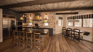 Una cocina moderna con una isla grande, piso de madera y una pared decorativa de piedra.