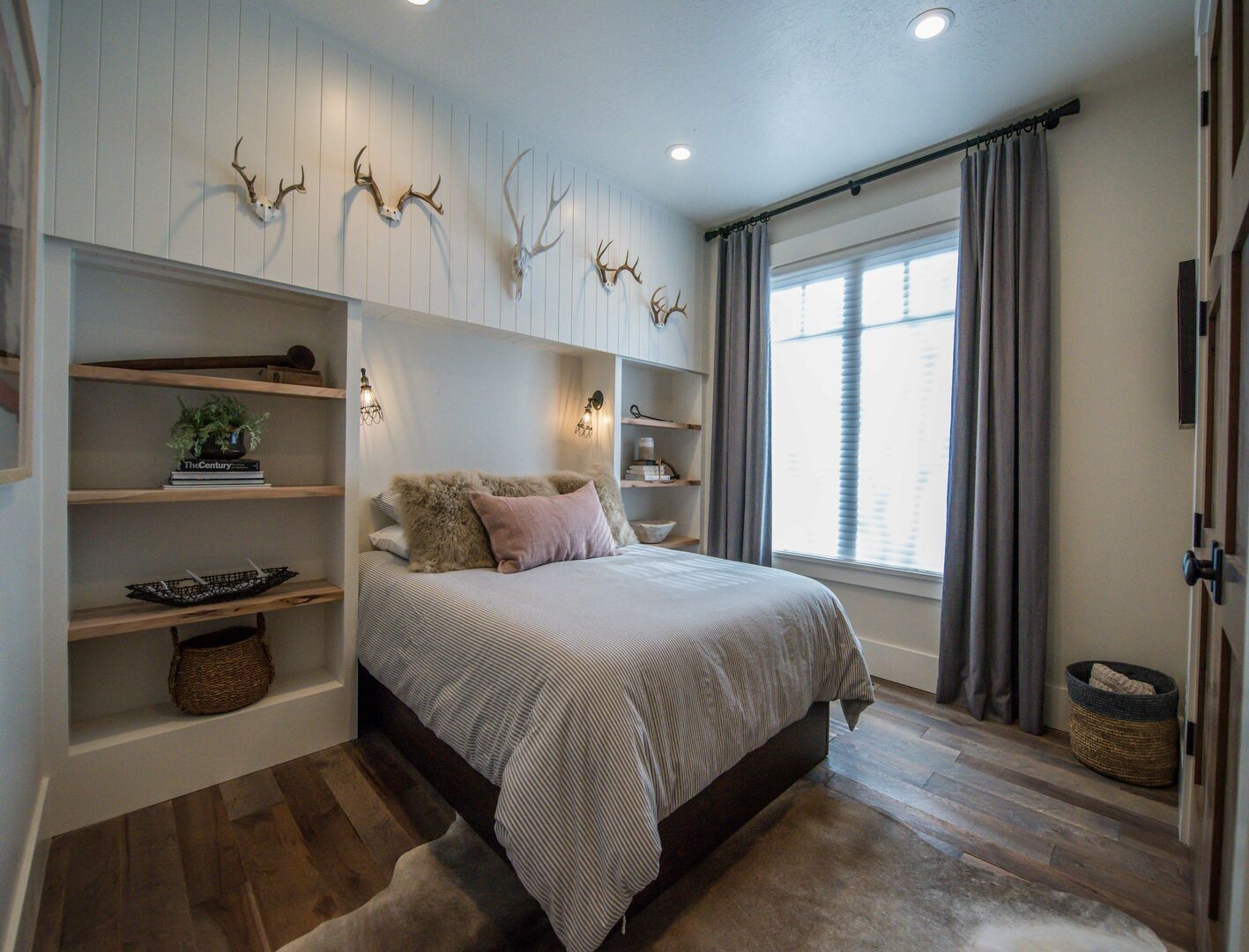A bedroom with a bed, shelves, and wall-mounted deer antlers.