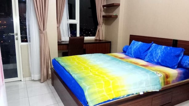 A bedroom with a bed, a desk, and a view of the city at night. - Apartemen Margonda Residence 4 & 5 by Liza (Depok)
