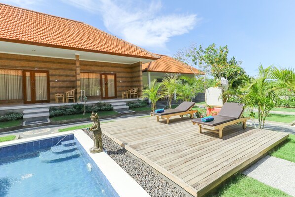 A wooden deck with two lounge chairs, a small pool, and a statue.