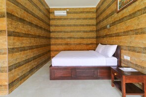 Habitación con cama en esquina, cabecera y mesita de noche de madera, y cubrecama blanco.