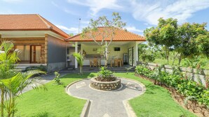 A house with a tiled roof, a circular garden with a central tree, and a well-maintained lawn. - Manik Homestay Uluwatu by Zuzu (Pecatu)