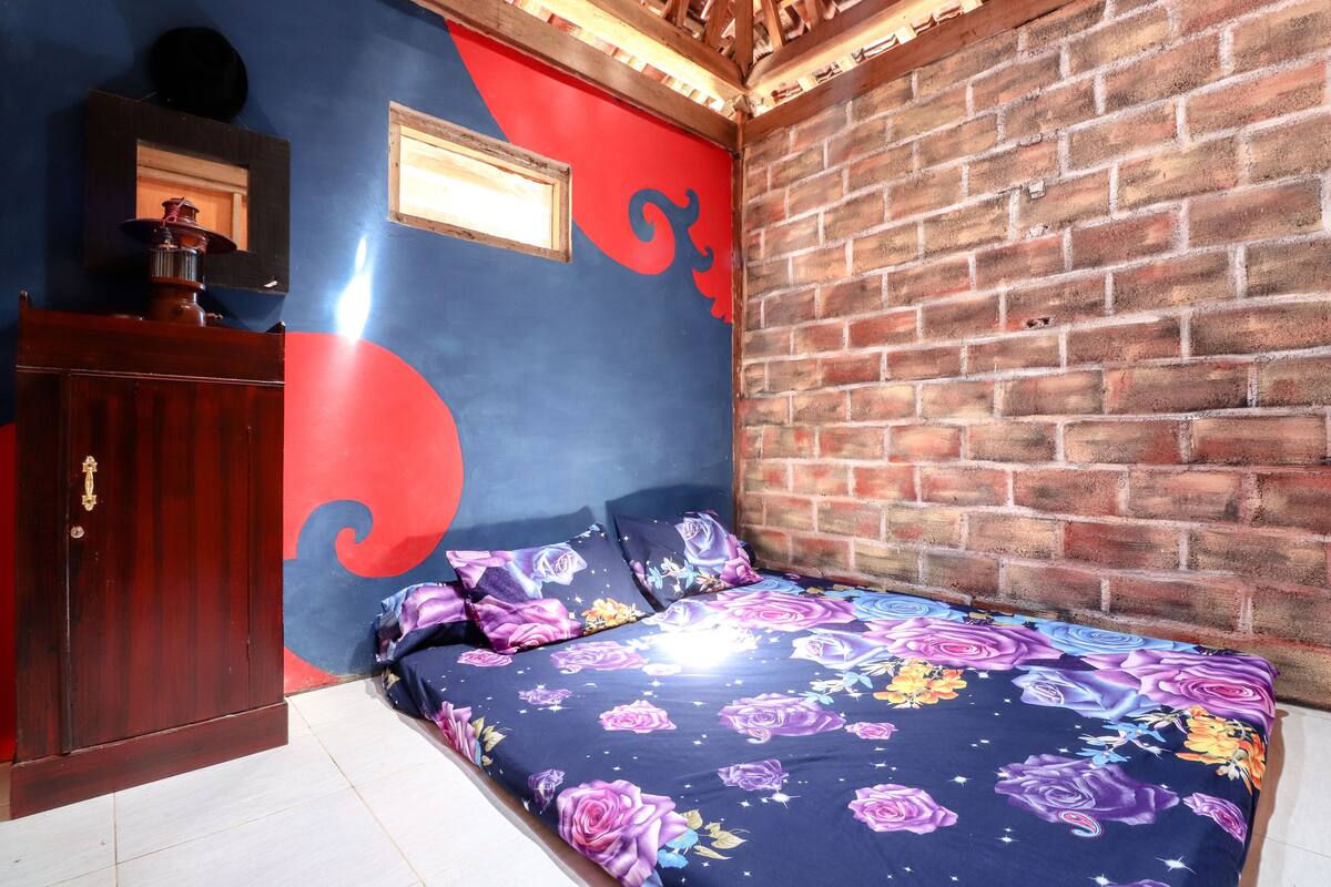 A bedroom with a brick wall, a wooden door, and a bed with floral bedding.