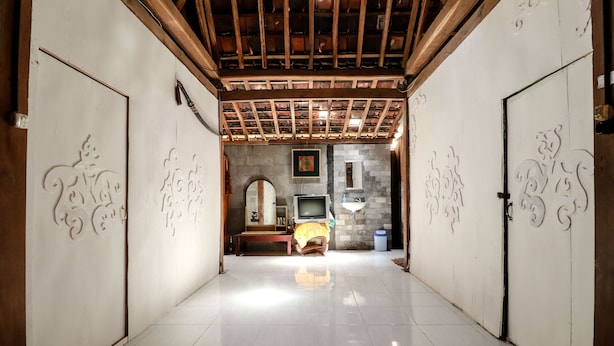 A hallway with a tiled floor, wooden ceiling beams, and decorative wall panels. - Segajih Central Stay and Education (Kokap)
