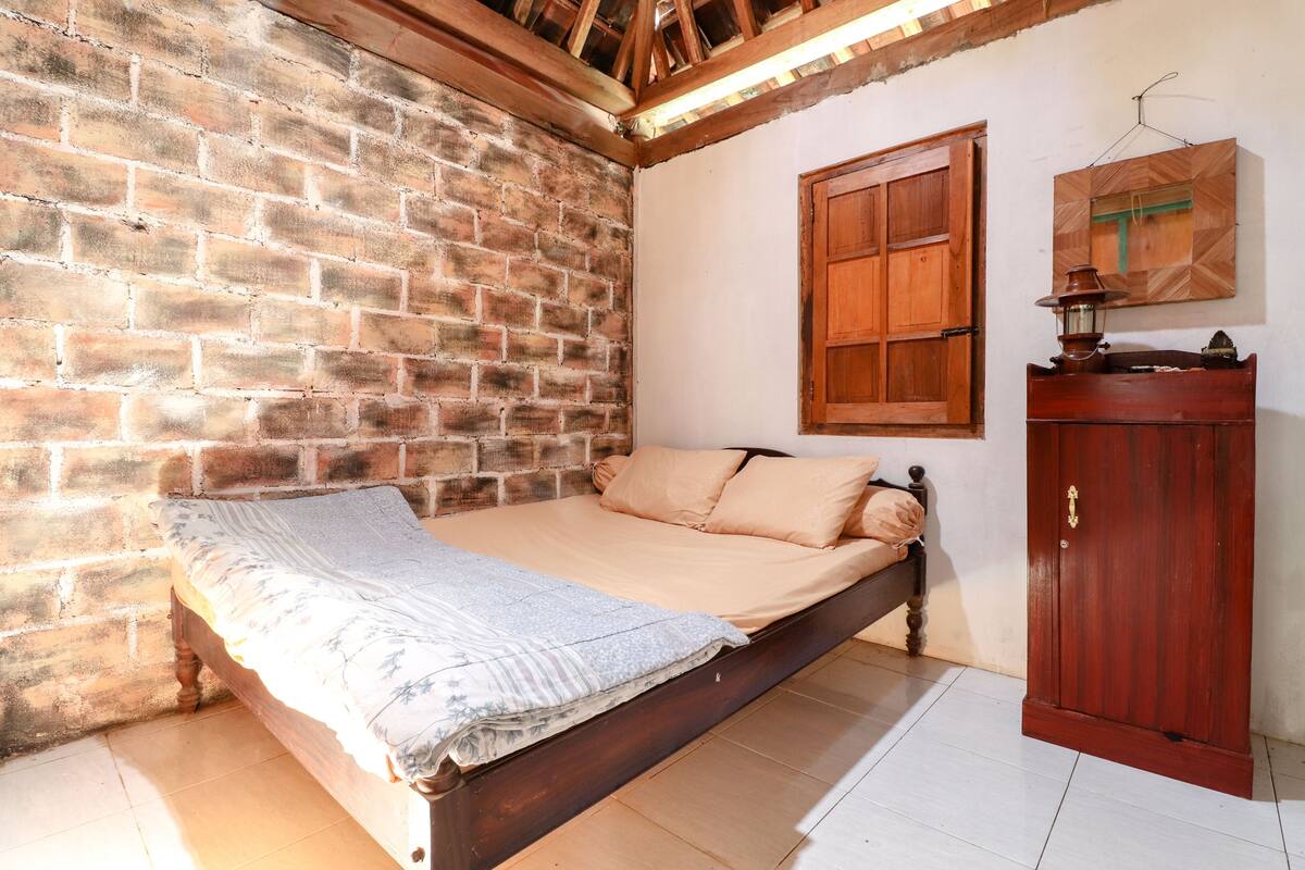 A room with a brick wall, a wooden bed, a wooden wardrobe, and a wooden cabinet.