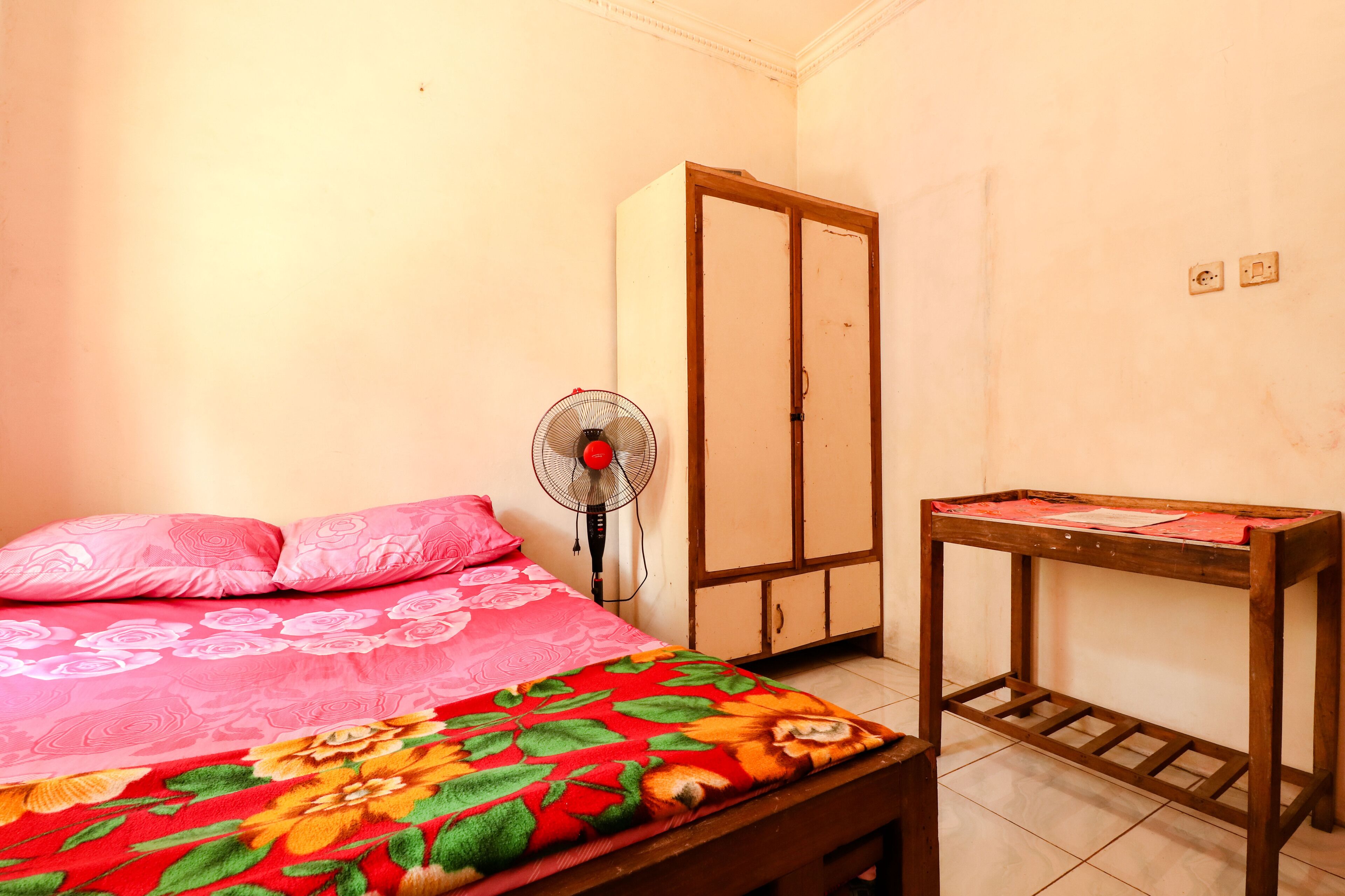 Un dormitorio con cama, armario, ventilador y mesa de madera.