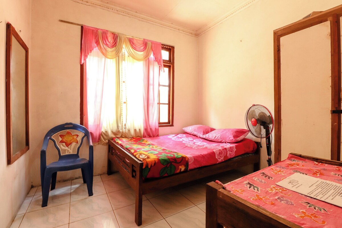 Un dormitorio con una cama, una silla, un ventilador y una mesa con un documento.