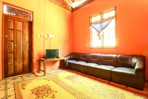 A room with a brown leather sofa, a wooden door, a small table with a lamp, and a window with curtains.