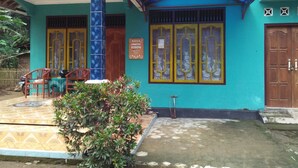 A building with a blue facade, a tiled porch, and a wooden door. - Sutrisno Homestay - Hostel (Kokap)