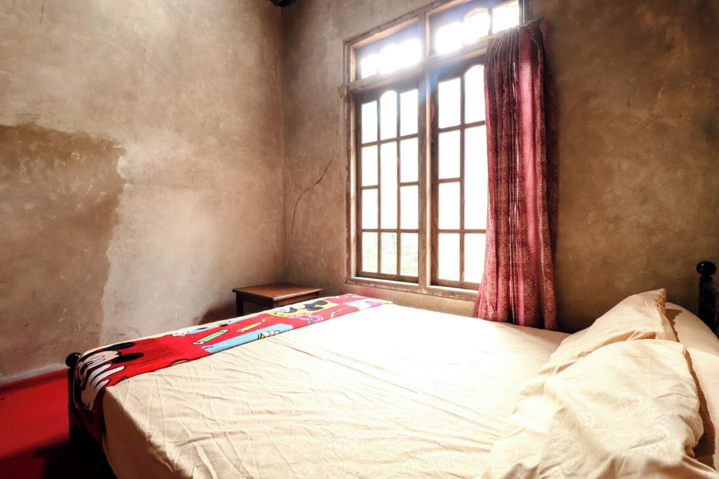 A room with a bed, a window with curtains, and a small table.