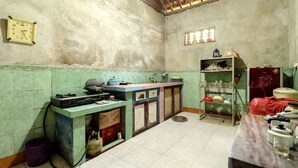 Uma cozinha com painel de azulejos, pia, bancada com diversos objetos e prateleira com louças.