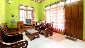 Sala de estar com televisão, móveis de madeira, um ventilador e uma janela grande com cortinas.
