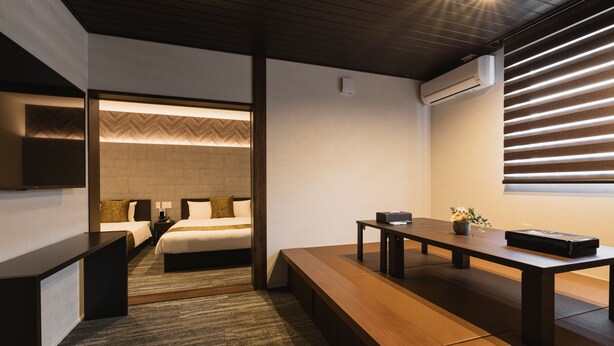 A modern hotel room with a wooden bench, a bed with a herringbone-patterned headboard, a bedside table, and a wall-mounted air conditioner. - GRAND BASE Crane (Fukuoka)