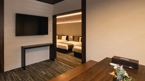 A hotel room with a TV mounted on the wall, a wooden console table, a bed with a headboard, and a bedside table with a tissue box and remote control. - GRAND BASE Crane (Fukuoka)