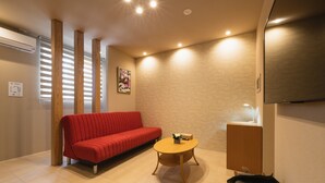 A modern living room with a red sofa, a wooden coffee table, and a television on a stand. - GRAND BASE Crane (Fukuoka)