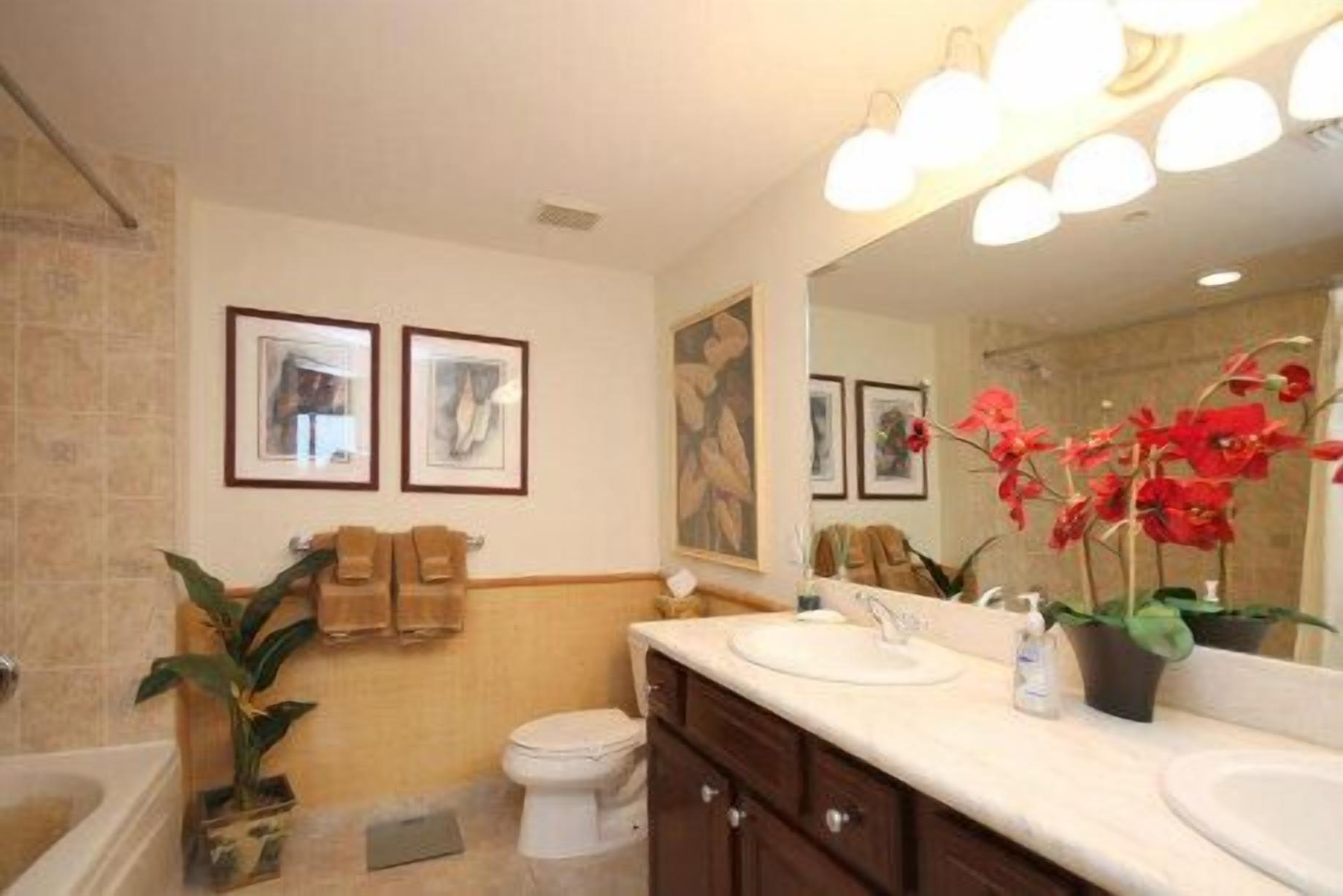 A bathroom with two sinks, a toilet, and a bathtub. There are framed pictures on the wall and a large mirror above the sink.