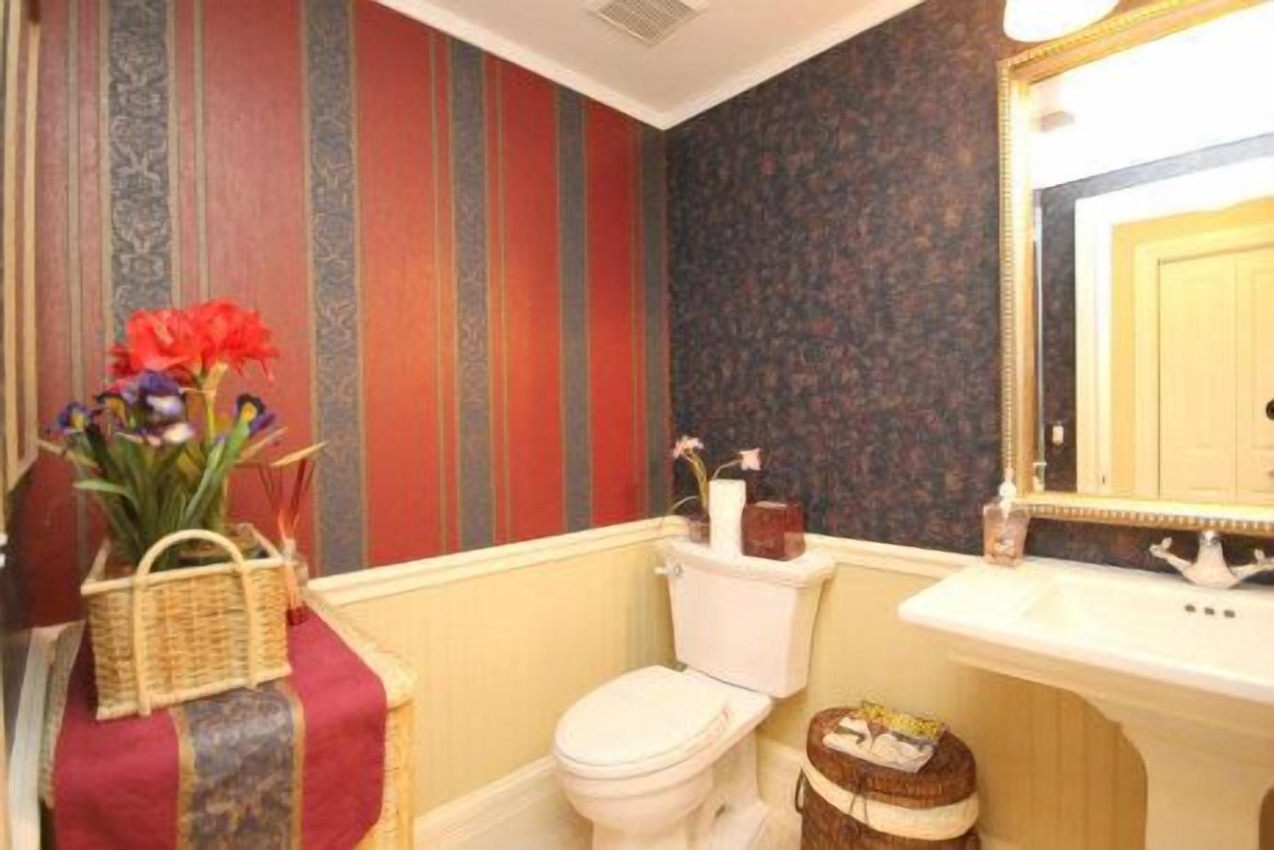 Een badkamer met streepjesbehang, een toilet, een wastafel en een spiegel.