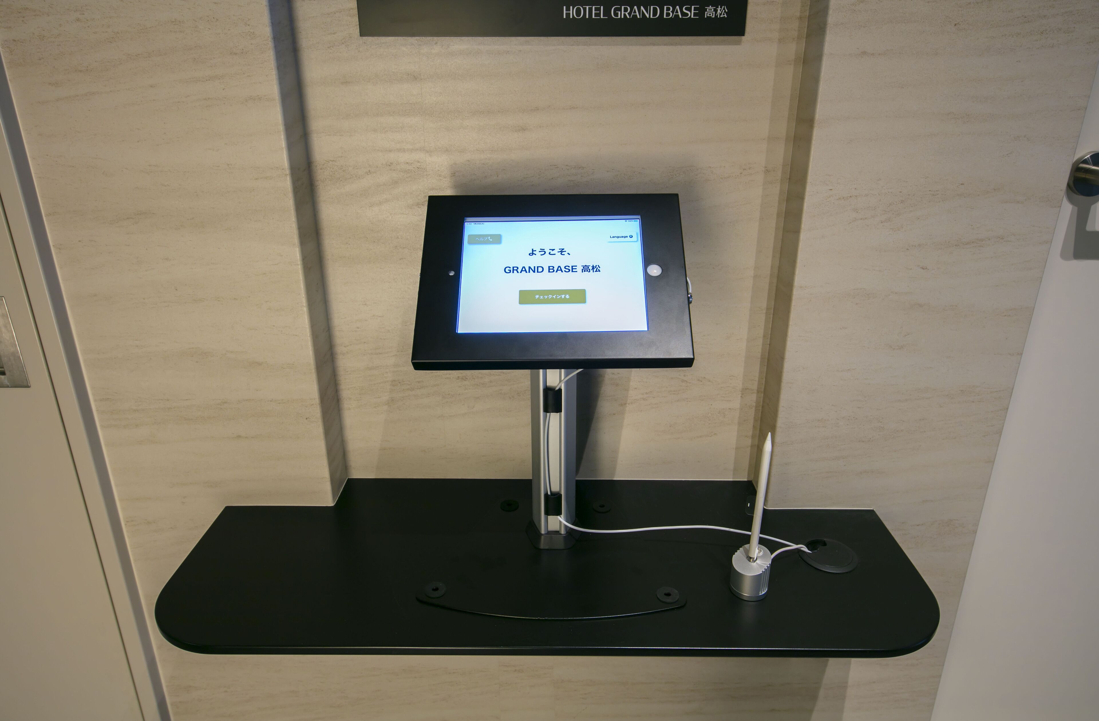 En digital informationskiosk med en skärm som visar texten ”GRAND BASE 高松” och en knapp under skärmen.