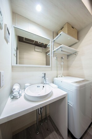 Ein modernes Badezimmer mit einem weißen Waschbecken, einem Spiegel und einem Handtuchhalter. Auf der Ablage befindet sich ein weißer Heizkörper und ein weißer Handtuchspender.