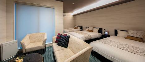 A hotel room with two beds, a sofa, a small table, and a window with blinds.