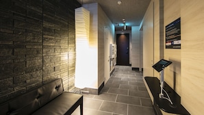 A hotel corridor with a dark brick wall, a bench, a reception desk, and a digital information kiosk.