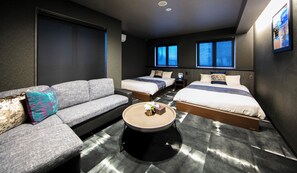 Ein modernes Hotelzimmer mit einem grauen Sofa, zwei Einzelbetten, einem runden Couchtisch und großen Fenstern.