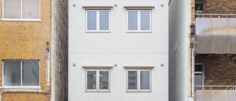 A multi-story building with a modern facade, a visible entrance, and a small garden area at the ground level.