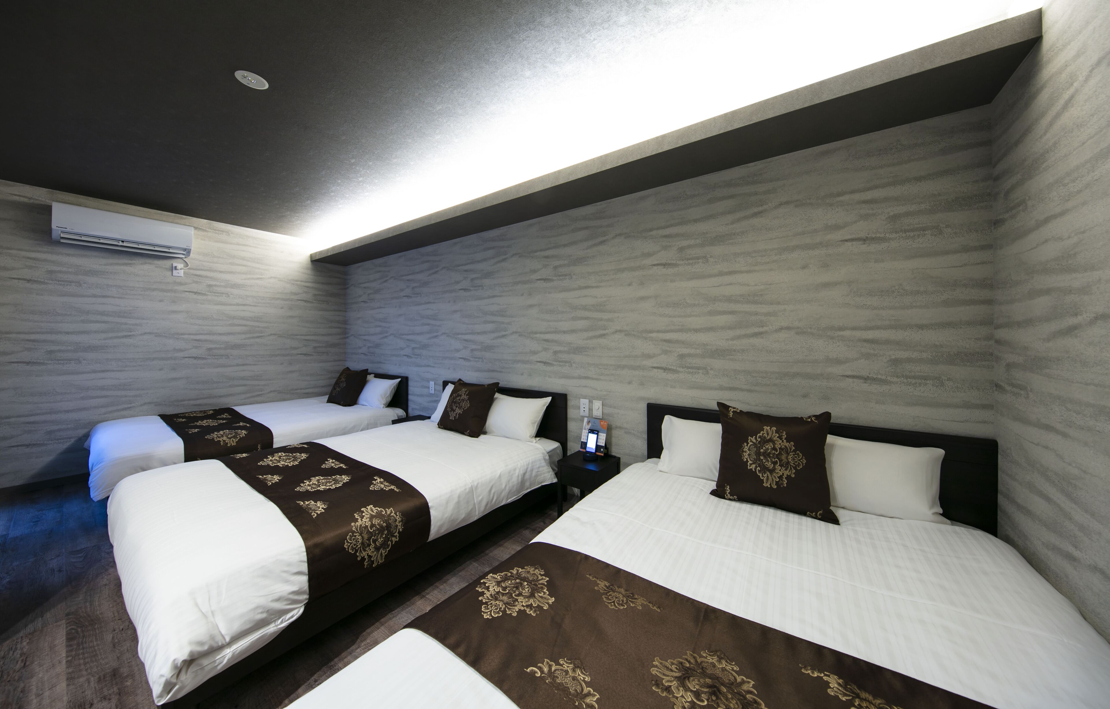 A hotel room with two beds, a nightstand with a phone and a card reader, and an air conditioning unit on the wall.