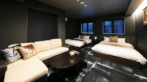 A hotel room with a sofa, two single beds, a small table, and a TV.