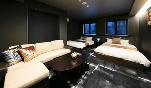 Quarto de hotel com sofá, duas camas de solteiro, uma mesinha e televisão.