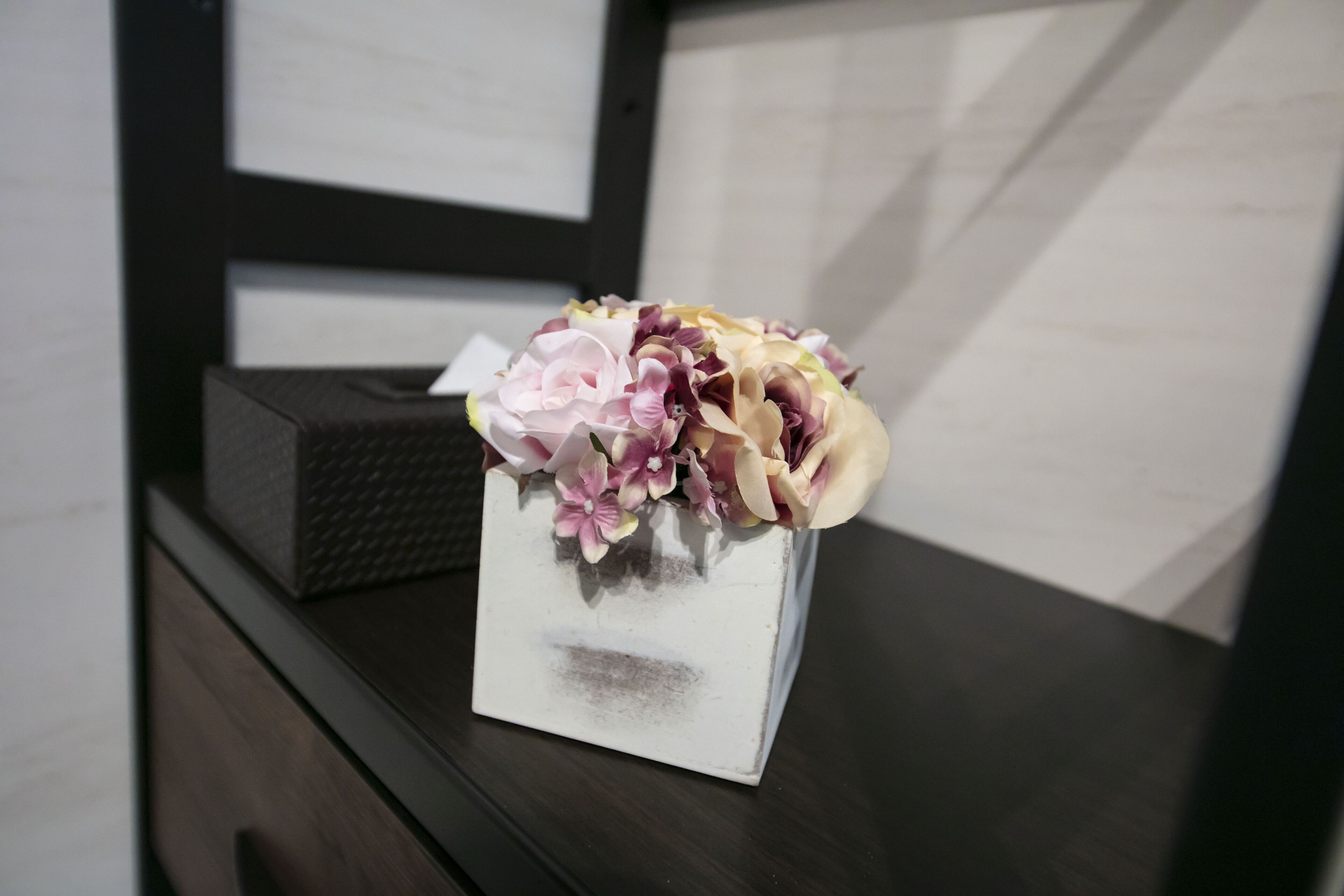 A white vase with flowers on a dark wooden dresser.