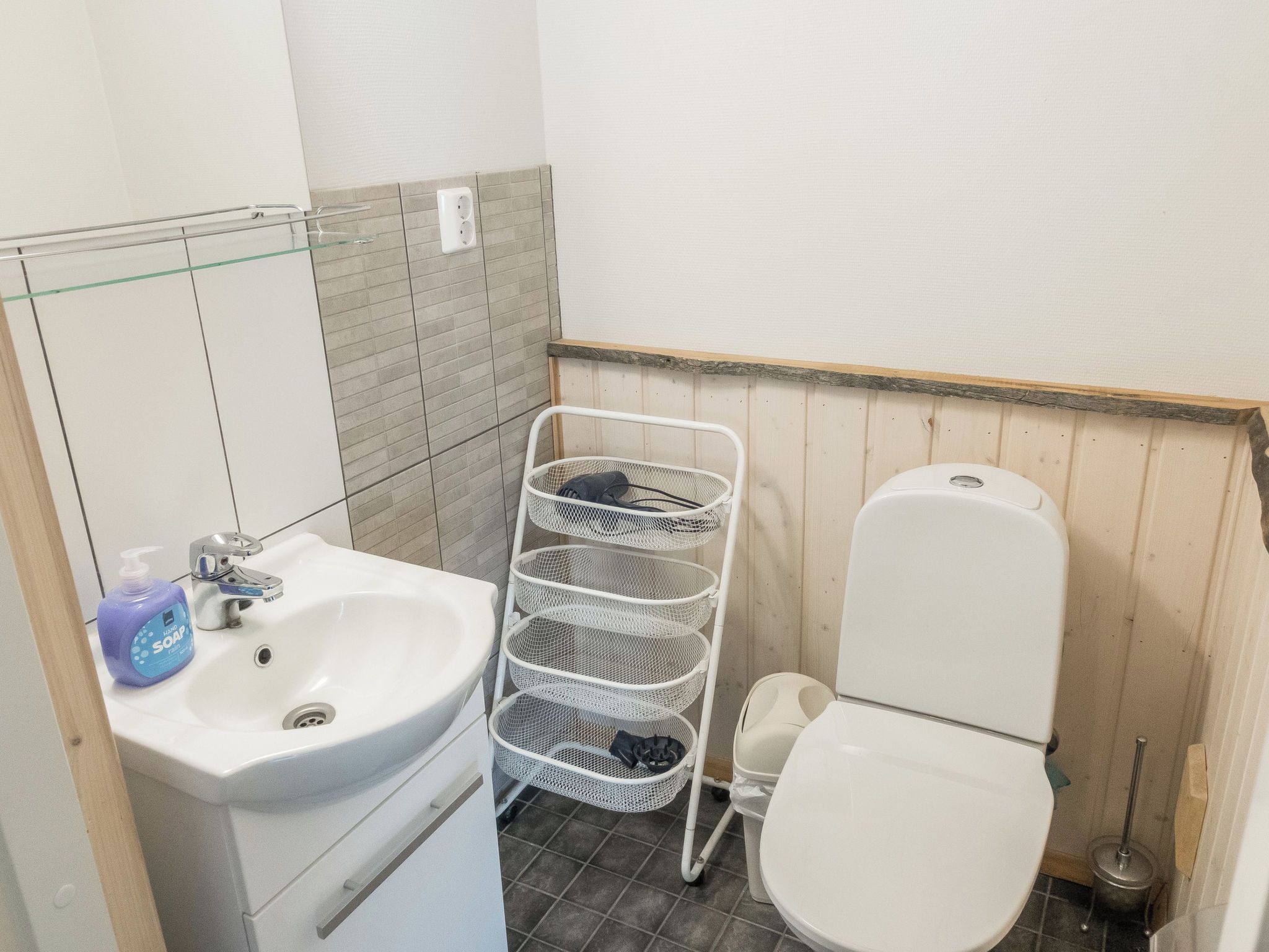 A small bathroom with a white sink, a toilet, and a metal basket rack.