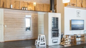 Een gezellige woonkamer met een open haard, houten wanden, een televisie en uitzicht op de zee.