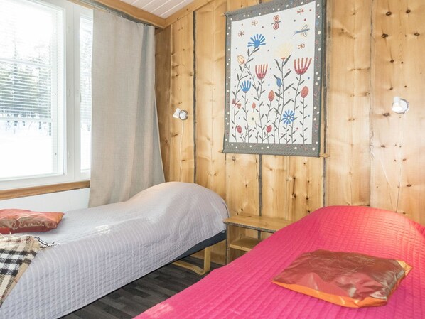 Une chambre avec deux lits, une fenêtre avec des rideaux et un mur orné d’une tapisserie à motifs floraux.