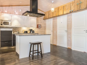 A modern kitchen with a central island, wooden cabinets, a built-in microwave, and a coffee machine. - Aarre a by Interhome (Inari)
