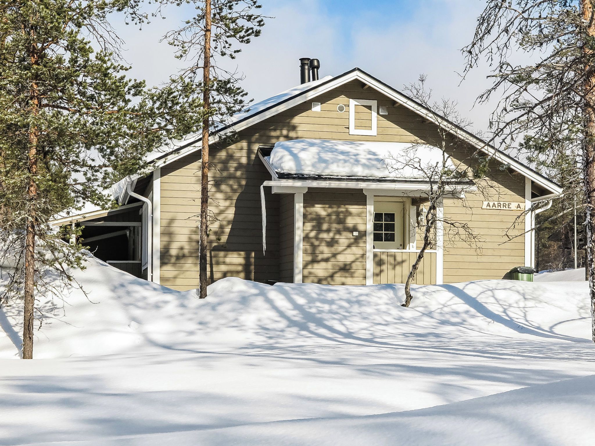 A wooden cabin with a snow-covered roof, surrounded by trees and a snow-covered ground.