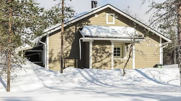 A wooden cabin with a snow-covered roof, surrounded by trees and a snow-covered ground.
