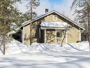 A wooden cabin with a snow-covered roof, surrounded by trees and a snow-covered ground.